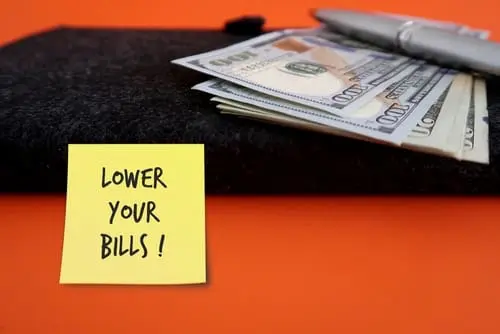 Black notebook, cash money dollars, pen and handwritten stick note LOWER YOUR BILLS