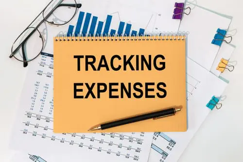 Notebook with the text Tracking Expenses on the office table among the stationery.