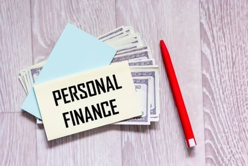 PERSONAL FINANCE text on a sticker with dollars and a red pen on a gray background