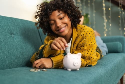 African American girl putting money coin in pink piggy bank.