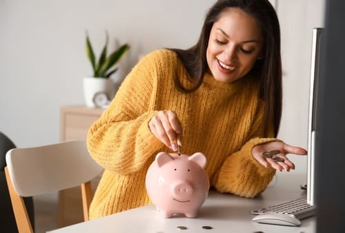 Young woman putting coin in piggy bank at home