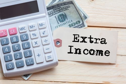 Extra Income Words on tag with dollar note and calculator on wood background