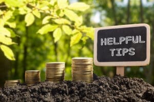 Helpful tips - Financial opportunity concept. Golden coins in soil Chalkboard on blurred urban background.
