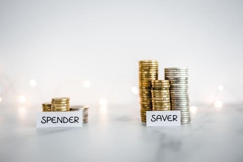 Saver vs spender texts in front of big and small stacks of coins.