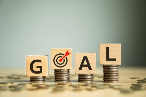 Wooden Block Letters Spelling "GOAL" Placed on Stacked Coins with Target Symbol, Representing Financial Goals, Ambition, and Strategic Planning for Success and Achievement