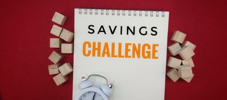 Take the Savings Challenge: Simple Steps to Grow Your Savings with Notebook, Wooden Cubes, and White Alarm Clock on a Red Background.